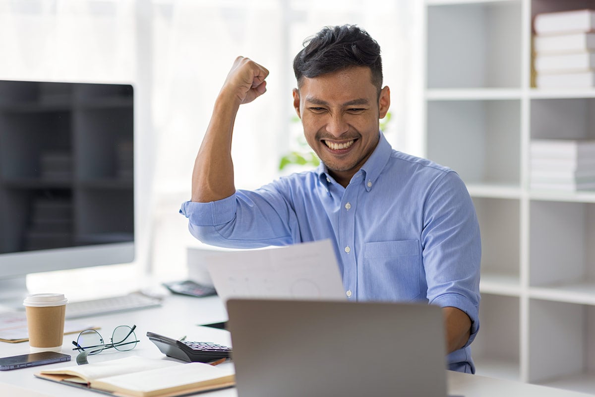 Asian man excited, celebrating at his desk Asian man excited, celebrating at his desk