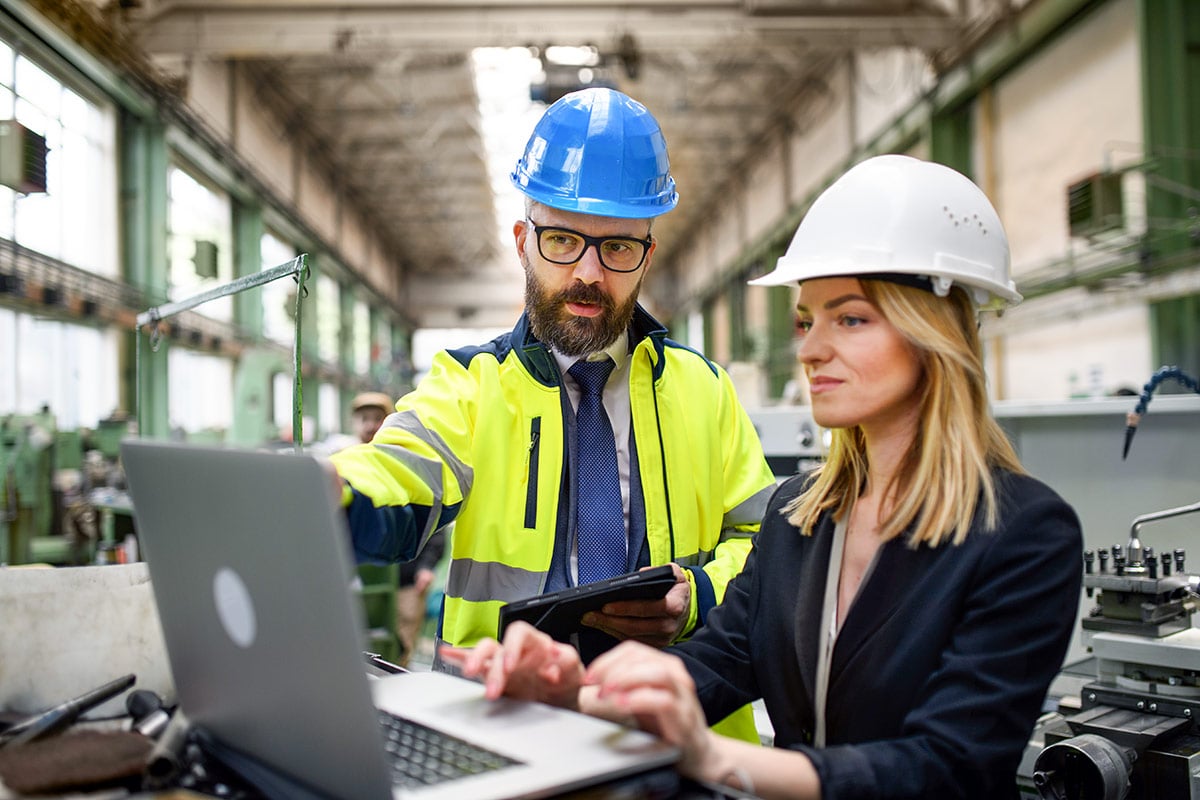 Male and female industrial engineers discussing factory's new machinery project and using laptop. Male and female industrial engineers discussing factory's new machinery project and using laptop.